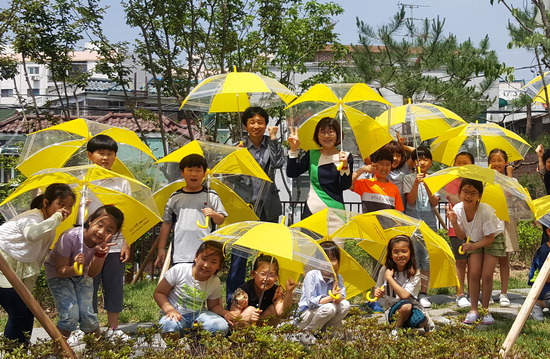 ▲ 수원시 파장초 3학년 학생들이 31일 ‘파장 안전 마을 만들기’ 현장에서 노란 우산을 쓰고 기념사진을 찍고 있다. 파장초 개교 80주년 기념공모를 통해 선정돼 제작된 우산은 노란색에 사이사이가 비닐이어서 비오는 날 시야를 밝게해 줘 안전사고 예방에 제격이다.  홍승남 기자 nam1432@kihoilbo.co.kr