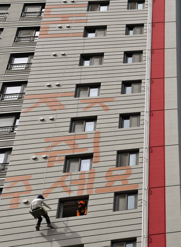 24일 화성시 반월동 신축 아파트 공사장 외벽에서 임금 체불 갈등을 빚는 도색업체 대표가 페인트로 ‘돈 주세요’라고 쓰면서 고공시위를 벌였다.   전광현 기자 jkh16@kihoilbo.co.kr